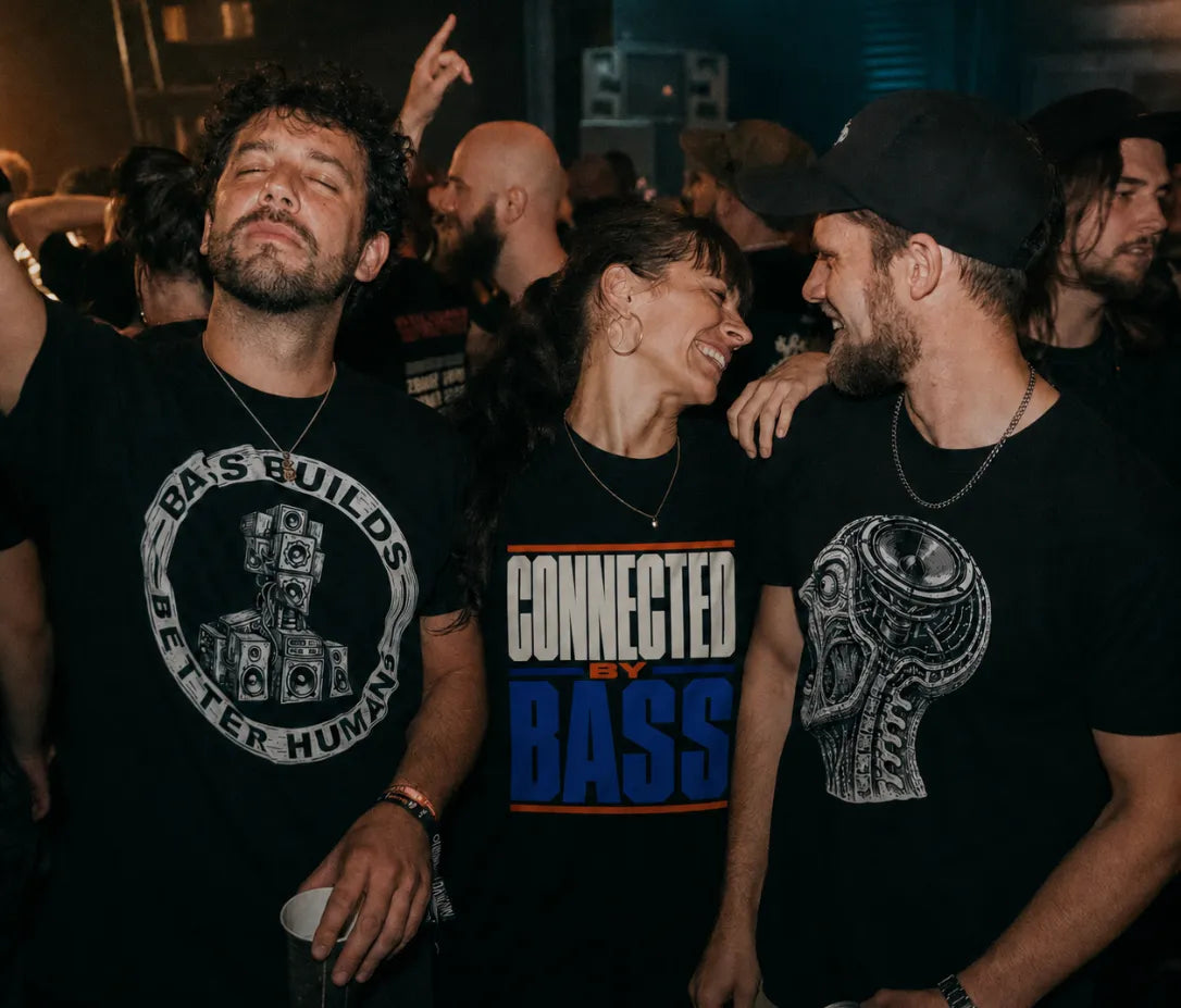 Three friends wearing black Drum and Bass graphic T-shirts together at an underground rave.