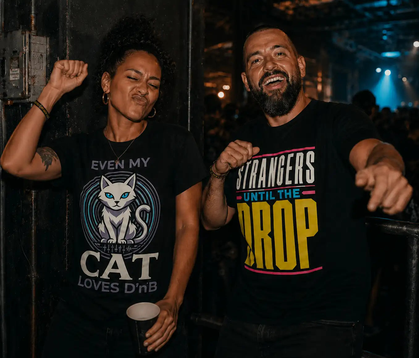 Two ravers dancing in black Drum and Bass graphic T-shirts at an underground bass music event.
